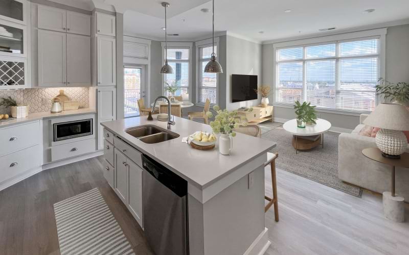 Furnished apartment kitchen with stainless steel appliances, floating kitchen island, and large windows in living area