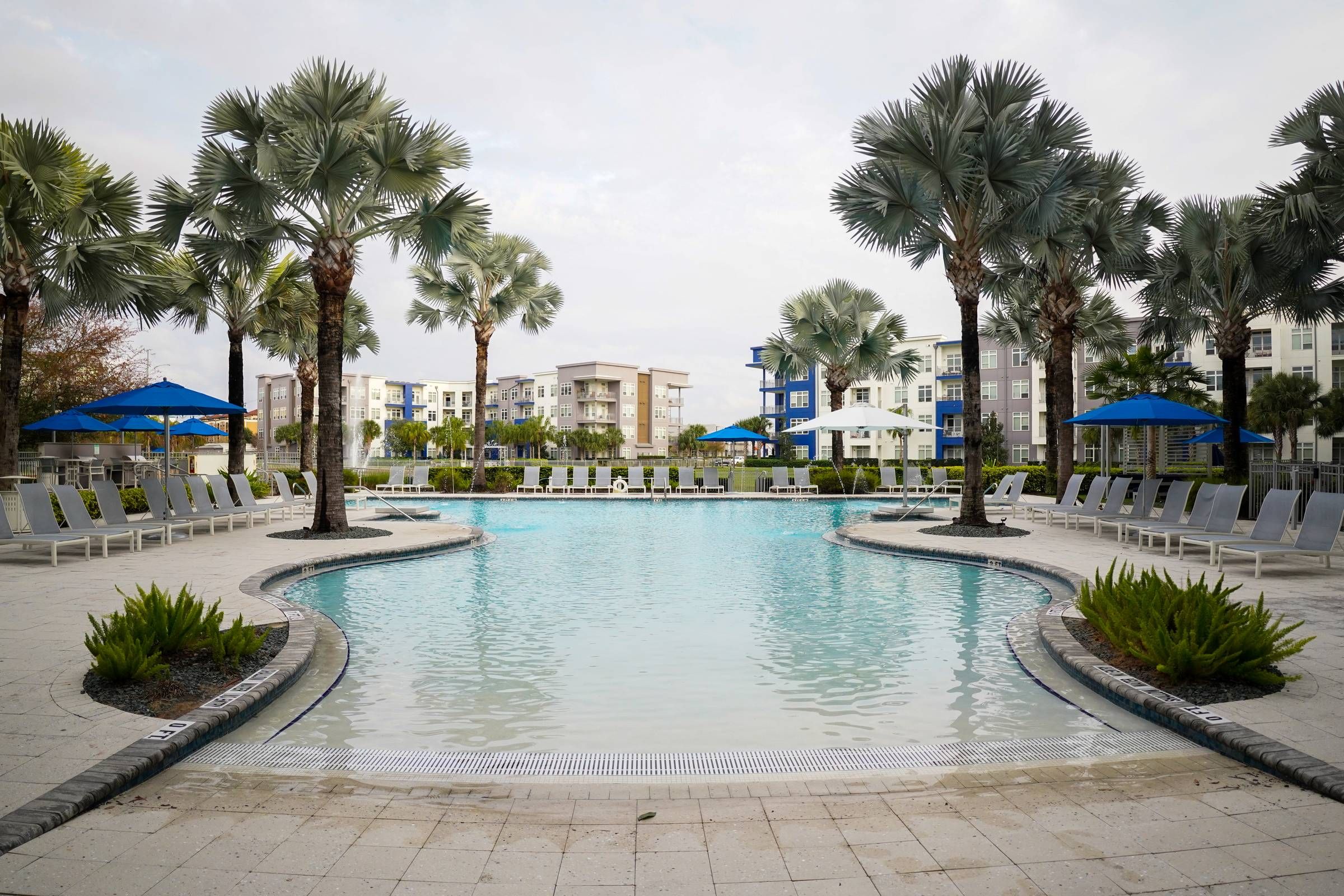 Inviting resort-style swimming pool at Solstice Apartments surrounded by palm trees and equipped with sun loungers and shaded areas for relaxation.