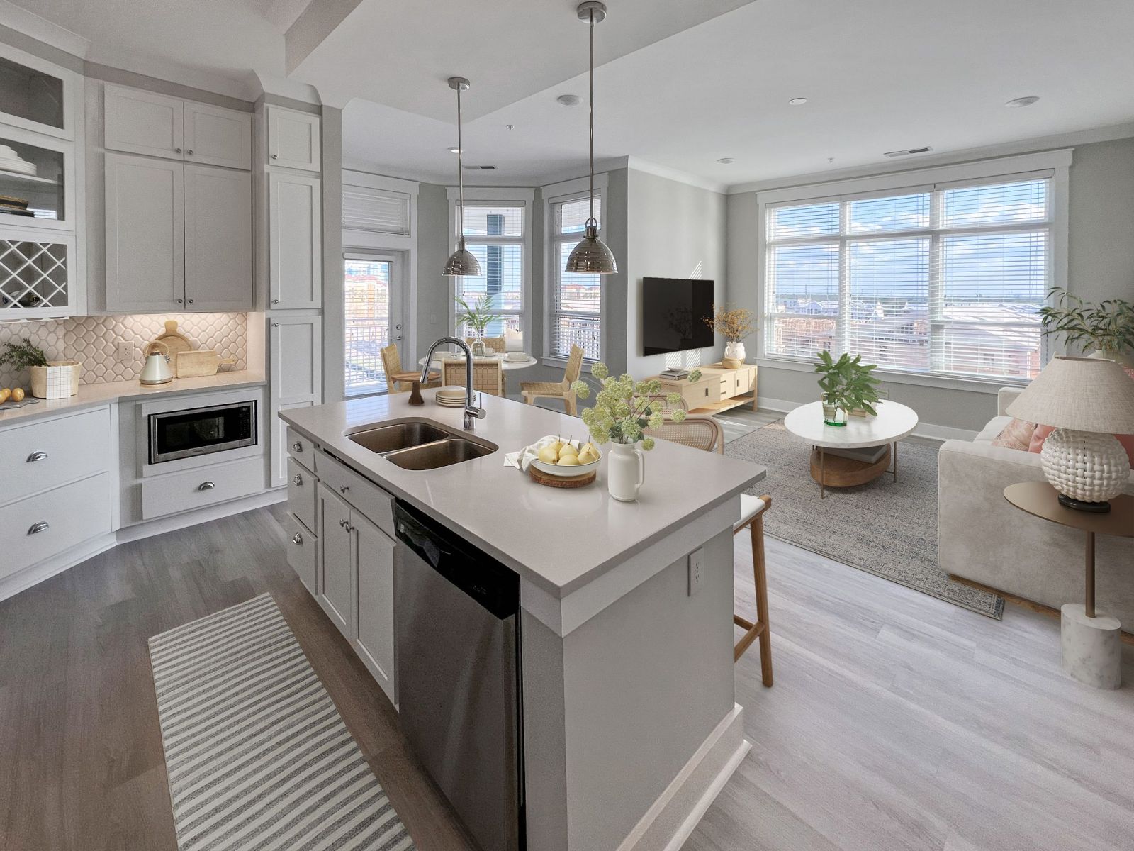 Contemporary kitchen in Solstice Apartments with white cabinetry, a central island, and stainless steel appliances, flowing into a brightly lit living area.