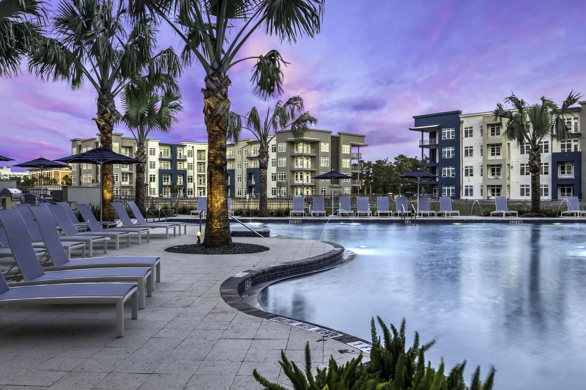 Solstice Apartments relaxing pool at sunset with ample lounge seating and palm tree landscaping.