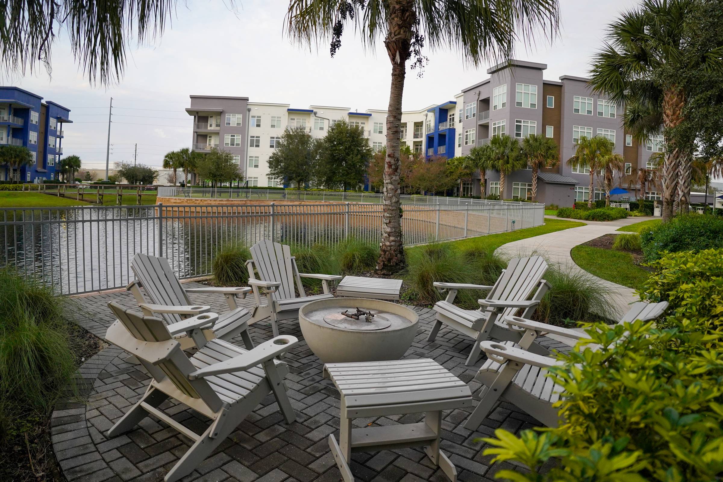 Solstice Apartments outdoor lounge area with Adirondack chairs circled around a fire pit with a lakeside view.