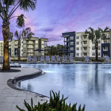 Solstice Apartments relaxing pool at sunset with ample lounge seating and palm tree landscaping.