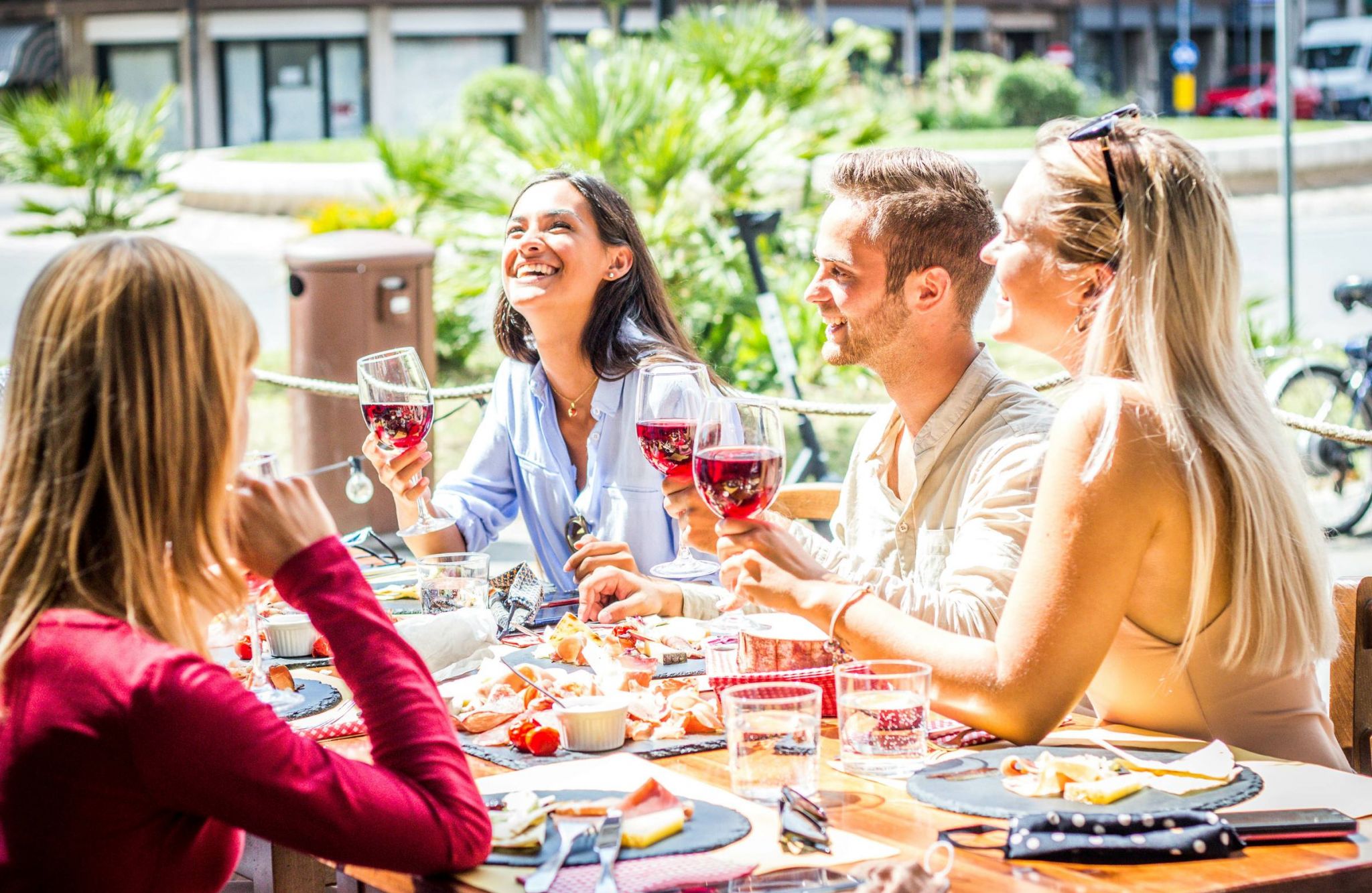 Group of friends dining outside at restaurant with wine and food on sunny day