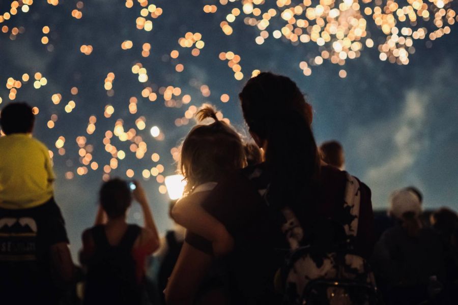 Mother and child watching firework display in night sky at theme park