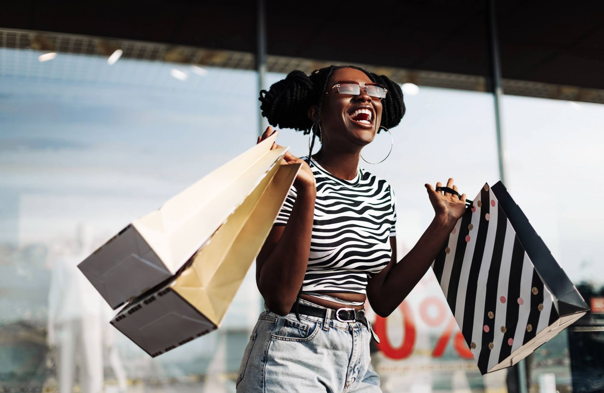 Woman wearing sunglasses, standing in a mall with shopping bags in her hands, enjoying shopping 