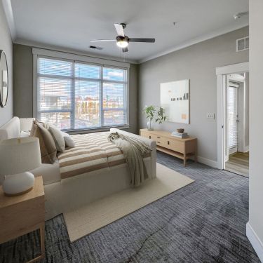 A serene bedroom at Solstice Apartments with a comfortable striped bed, modern furnishings, and a window offering ample natural light.
